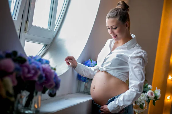 Gravid glad kvinna röra hennes mage. Gravid ung mamma porträtt, smekande hennes mage och leende. Frisk graviditet koncept, brunett gravid kvinna nära fönstret — Stockfoto