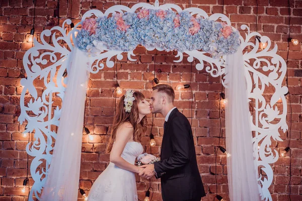 Retrato de noiva jovem feliz e noivo em um interior clássico perto do arco de casamento com flores. Dia do casamento, tema do amor. Primeiro dia de uma nova família — Fotografia de Stock