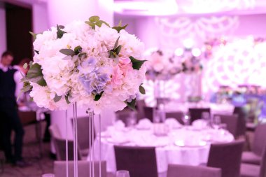 Bir parti, düğün resepsiyon veya diğer festival olay için yüksek bir kök üzerinde bir vazo tabak ve beyaz çiçek düzenlemeleri ile güzel masa ayarı. Catered etkinlik yemeği için cam eşya ve çatal bıçak takımı