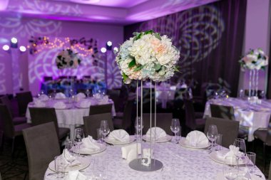 Bir parti, düğün resepsiyon veya diğer festival olay için yüksek bir kök üzerinde bir vazo tabak ve beyaz çiçek düzenlemeleri ile güzel masa ayarı. Catered etkinlik yemeği için cam eşya ve çatal bıçak takımı