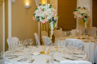 Bir parti, düğün resepsiyon veya diğer festival olay için yüksek bir kök üzerinde bir vazo tabak ve beyaz çiçek düzenlemeleri ile güzel masa ayarı. Catered etkinlik yemeği için cam eşya ve çatal bıçak takımı