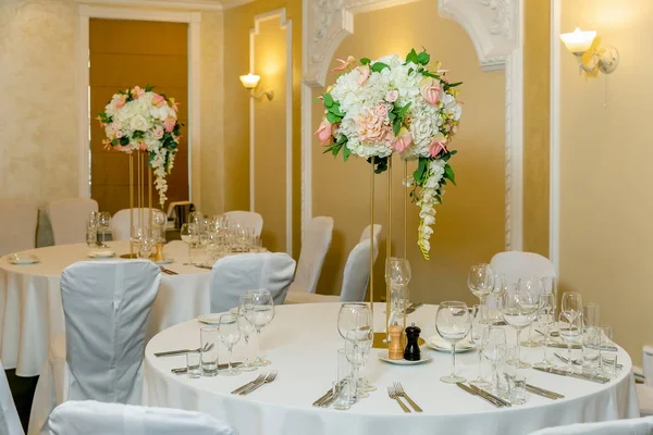 Bir parti, düğün resepsiyon veya diğer festival olay için yüksek bir kök üzerinde bir vazo tabak ve beyaz çiçek düzenlemeleri ile güzel masa ayarı. Catered etkinlik yemeği için cam eşya ve çatal bıçak takımı
