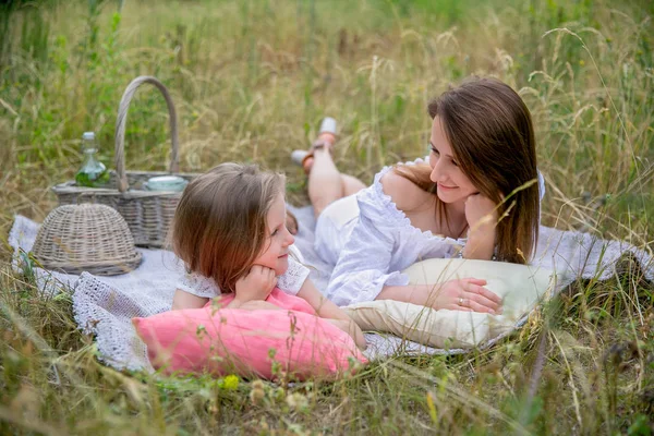 Красива молода мати і її маленька дочка в білій сукні розважаються на пікніку. Вони лежать на плоскогір'ї на траві і посміхаються. Догляд за дітьми та кохання. Горизонтальна фотографія — стокове фото