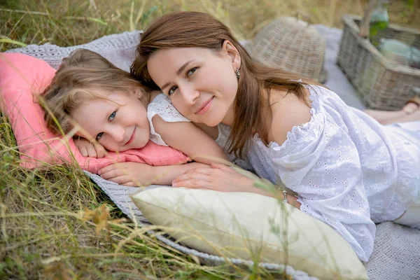 Krásná mladá matka a její dceruška v bílých šatech se baví na pikniku. Leží na plna trávy, objetí a usmívající se. Mateřská péče a láska. Vodorovná fotografie — Stock fotografie