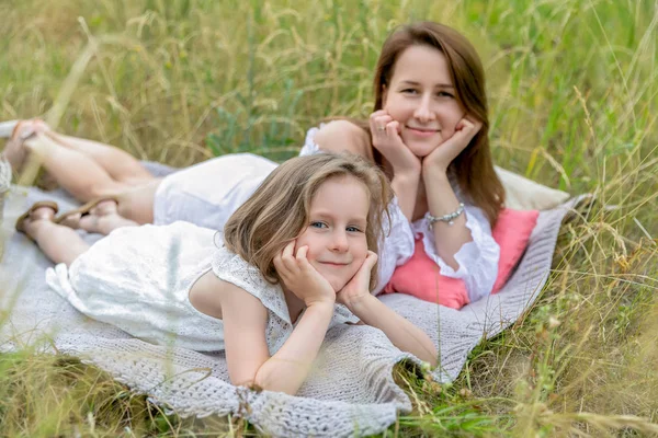 Красива молода мати і її маленька дочка в білій сукні розважаються на пікніку. Вони лежать на плоскогір'ї на траві і посміхаються. Догляд за дітьми та кохання. Горизонтальна фотографія — стокове фото