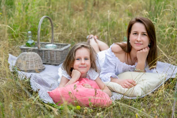 Krásná mladá matka a její dceruška v bílých šatech se baví na pikniku. Leží na plna trávy a usmívají se. Mateřská péče a láska. Vodorovná fotografie — Stock fotografie