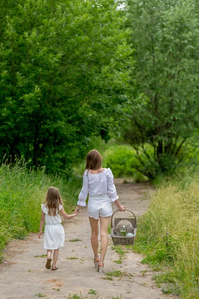 Красива молода мати і її маленька дочка в білій сукні розважаються на пікніку. Вони ходять по дорозі в парку. Догляд за дітьми та кохання. Вертикальне фото — стокове фото