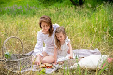 Otuz yaşında güzel genç anne ve beyaz elbiseli küçük kızı piknikte eğleniyor. Çimenlerin üzerinde bir ekose üzerinde oturuyorlar ve sandviç leri çıkarıyorlar. Anne bakımı ve sevgi