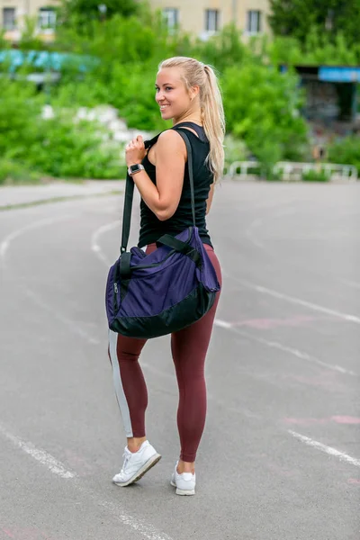 フィットネスライフスタイル。スポーツバッグを持つ運動の若い女性は、トレーニングの後に立っています。バックビュー。スタジアムでのワークアウト。健康的な生活の概念 — ストック写真