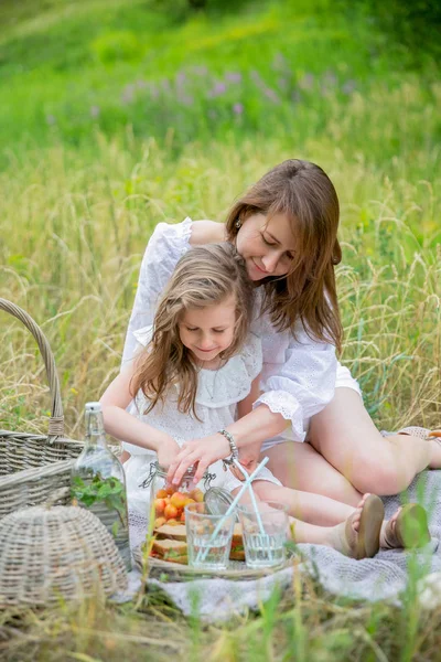 Piękna młoda matka i jej mała córka w białej sukni zabawy w Pikniku. Siedzą na chodnik i wziąć jagody z słoika. Macierzyńską opiekę i miłość. Zdjęcie verticalal — Zdjęcie stockowe