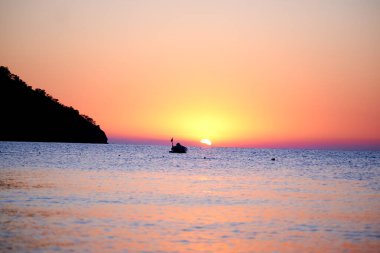 Denizin üstünde turuncu gün batımı ve sakin dalgalarda güneşin altın yansıması.