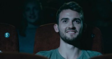 Gülümseyerek, keyfi bir sinema oturan genç adam.
