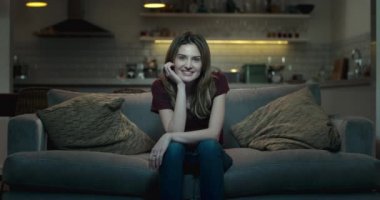 Geceleri rahat bir oturma odasında TV izlerken çok mutlu bir gülümseyen kadın.