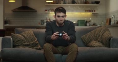 Genç adam kanepede oturmuş video oyunları oynuyor..