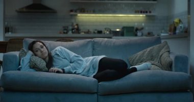 Genç kadın gece televizyon izlerken rahat bir kanepede uzanmış