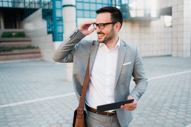 Gülümseyen ve dışında iş çizelgeleri tutan bir işletme Binası önünde duran genç başarılı iş adamı.