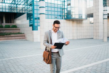 Gülümseyen ve dışında iş çizelgeleri tutan bir işletme Binası önünde duran genç başarılı iş adamı.