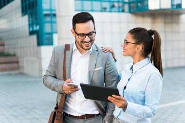 Birlikte çalışan genç başarılı iş, tablet kullanma ve bir iş sahip bir cam bina önünde derler.