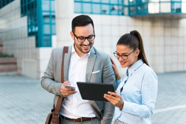 Birlikte çalışan genç başarılı iş, tablet kullanma ve bir iş sahip bir cam bina önünde derler.