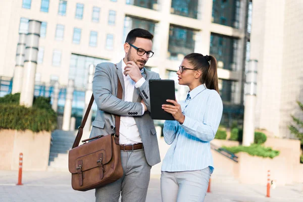 Young business people talking, working together using tablet and business plans, standing outside in front of a business center.