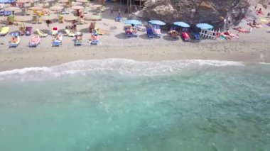 La Spezia, İtalya 'daki Cinque Terre' nin Monterosso al Mare köyünün panorama manzarası. Kumsal boyunca uçmak, şemsiyeler, insanlar, evler görünür. 4K video