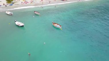 La Spezia, İtalya 'daki Cinque Terre' nin Monterosso al Mare köyünün panorama manzarası. İnsansız hava aracı kıyıdan uzaklaşır ve insanlar yakını ve denizi teknelerle ağlarken görülebilir..