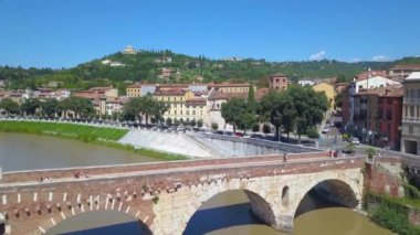 İtalya, Verona 'nın panoramik hava aracı görüntüsü. İnsansız hava aracı Ponte Pietra köprüsünden uzaklaşır ve nehir kenarındaki araba trafiğini görür. 4K içinde video