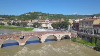 İtalya, Verona 'nın panoramik hava aracı görüntüsü. İnsansız hava aracı Ponte Pietra köprüsünden uzaklaşır ve nehir kenarındaki araba trafiğini görür. 4K içinde video