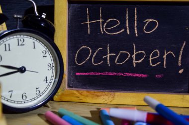 Yazı tahtası üzerinde el yazısı Ekim'de ifade renkli Merhaba. Eğitim ve iş kavramı. Çalar saat, tebeşir, siyah arka plan üzerine kitaplar