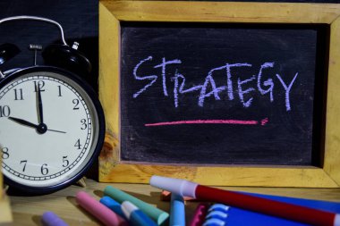 Strateji ifade renkli yazı tahtası üzerinde el yazısı üzerinde. Eğitim ve iş kavramı. Çalar saat, tebeşir, siyah arka plan üzerine kitaplar