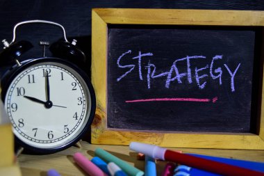 Strateji ifade renkli yazı tahtası üzerinde el yazısı üzerinde. Eğitim ve iş kavramı. Çalar saat, tebeşir, siyah arka plan üzerine kitaplar