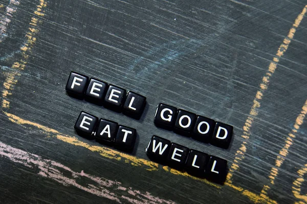 Feel Good Eat Well on wooden blocks. Cross processed image with blackboard background. Inspiration, education and motivation concepts