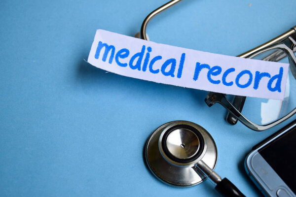 Conceptual image with Medical record inscription with the view of stethoscope, eyeglasses and smartphone on the blue background. Medical Conceptual.