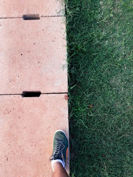 man step up on right foot in green sneaker. cement drain grate and green grass with abstract background