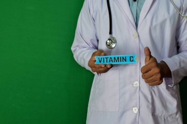 Yeşil arka planda duran doktor. C vitamini kağıt metnini tutun. Tıp ve sağlık kavramı.