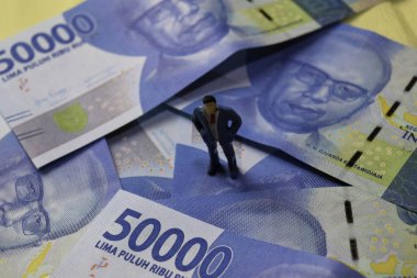 Miniature people standing on Indonesian Rupiah with world economics and inflation control concept