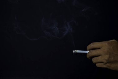 Siyah arka planda sigara tutan Asyalı bir adamın eli. Sigara içme kavramı