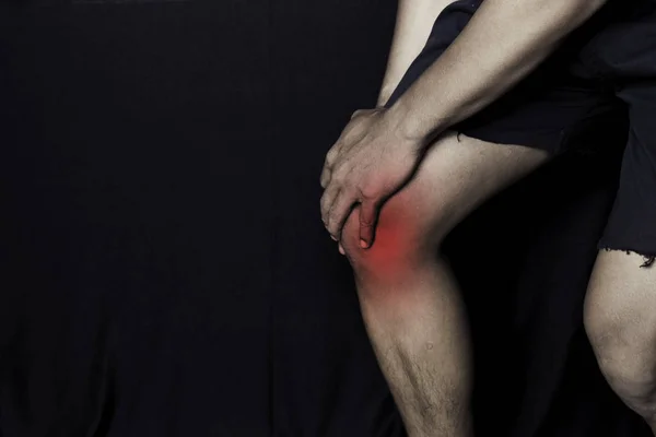Азіат тримає коліно. Він відчуває біль на коліні з чорним фоном. Об'єднане запалення або концепція охорони здоров'я — стокове фото