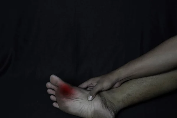 Азіат тримає ногу. Він відчуває біль від кукурудзи на нозі з чорним фоном. Концепція медичної або медичної допомоги — стокове фото