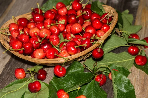 Tahta arka planda yaprakları olan bir sepet tatlı ve olgun kiraz.