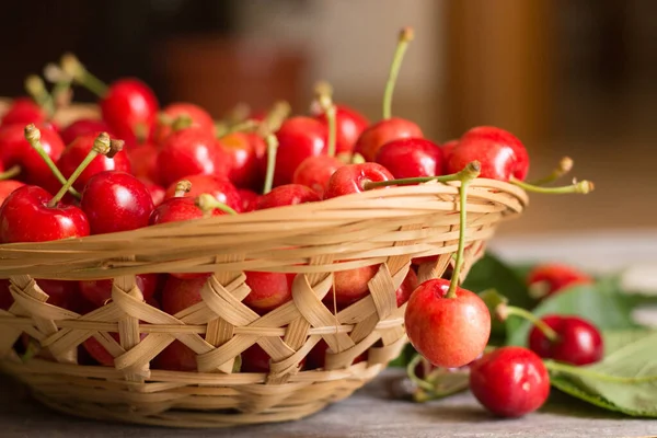 Basket of sweet and ripe cherries with leaves on wooden background