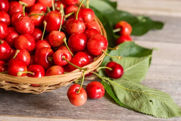 Tahta arka planda yaprakları olan bir sepet tatlı ve olgun kiraz.