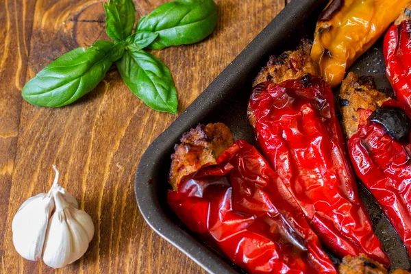 Doldurulmuş biberin vejetaryen versiyonu fırında pişiyor. Tahta arka planda fesleğen ve sarımsaklı