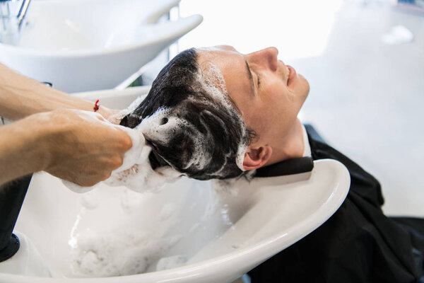 Profile view of a young man getting his hair washed and his head massaged in a hair salon