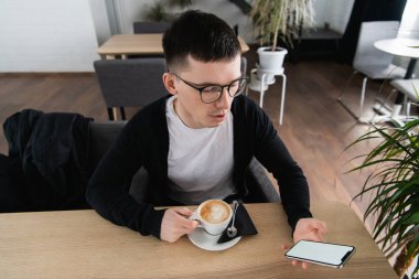 Genç adam tutarak hareket eden telefon. Restoran veya Cafe oturuyor. Bir video ya da film izlemeye çalışıyorum. Reklam veya logo için yer