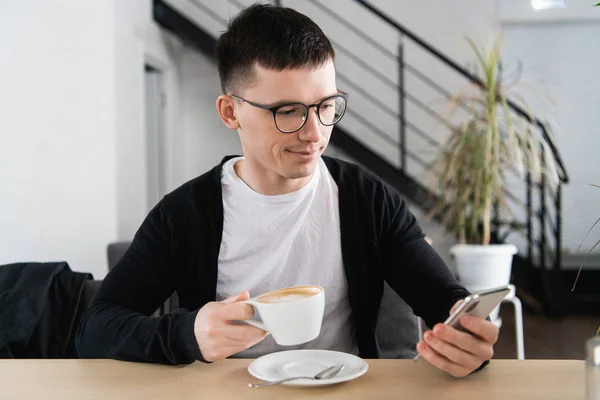 Handsome man having coffee and using smartphone at coffee shop