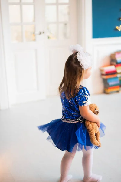 Menina muito pequena em belo vestido azul de pé para trás e segurando seu brinquedo — Fotografia de Stock