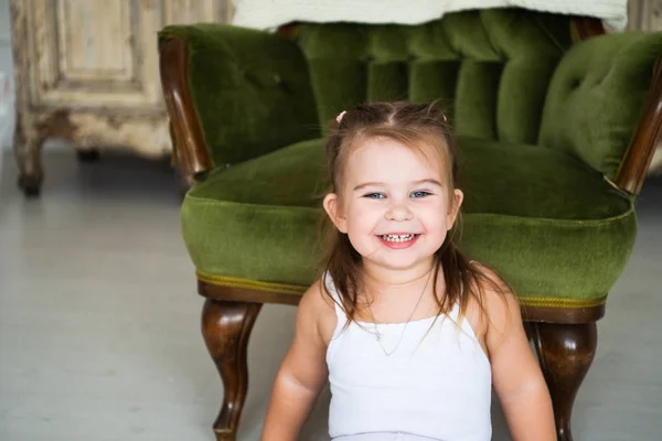 Retrato de uma menina rindo feliz sentada no chão perto da cadeira antiga — Fotografia de Stock