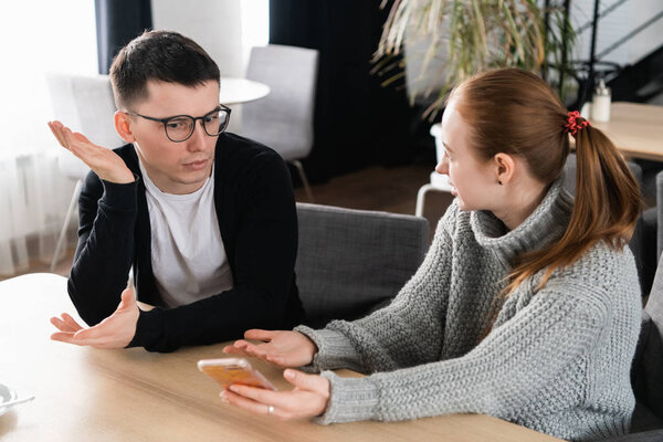 Girlfriend asking for explanation of her boyfriend sitting on a couch in the cafe