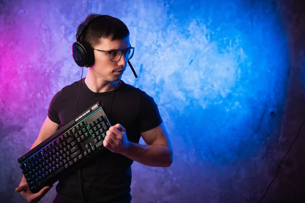 Professional Boy Gamer hospodářství herní klávesnice přes barevné neon růžové a modré osvětlené zdi. Herní hráči koncept — Stock fotografie